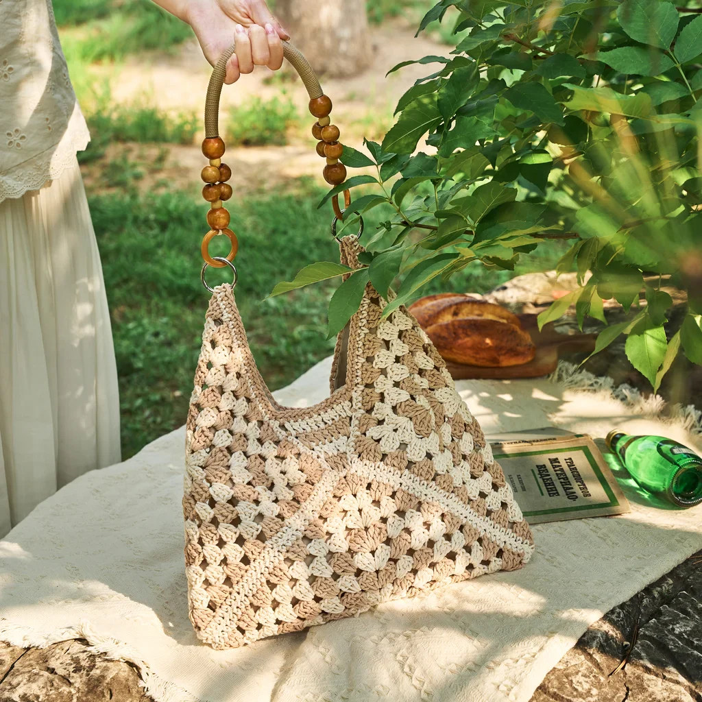 Beige crochet bag with wooden bead handles on outdoor picnic blanket — handmade summer tote in garden setting