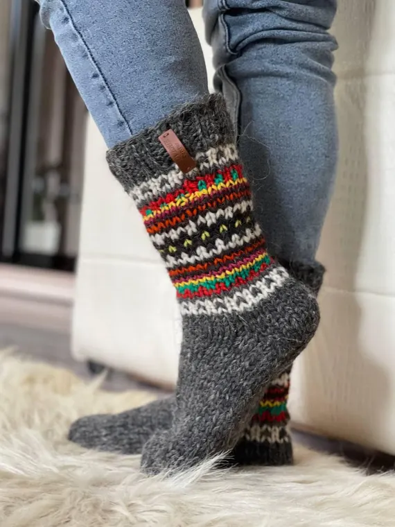 Hand-knit grey wool slipper socks with colorful Nordic fair-isle pattern — warm chunky house footwear on sheepskin rug