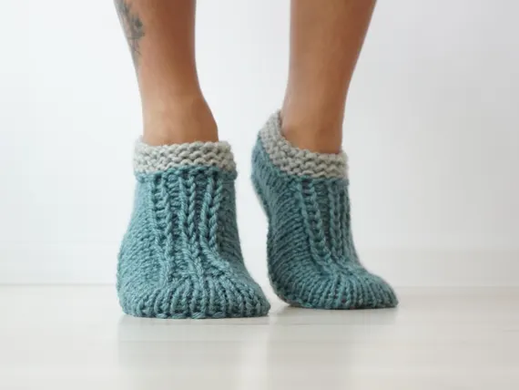 alt="Cozy teal hand-knitted merino wool slippers with grey cuffs worn at home"