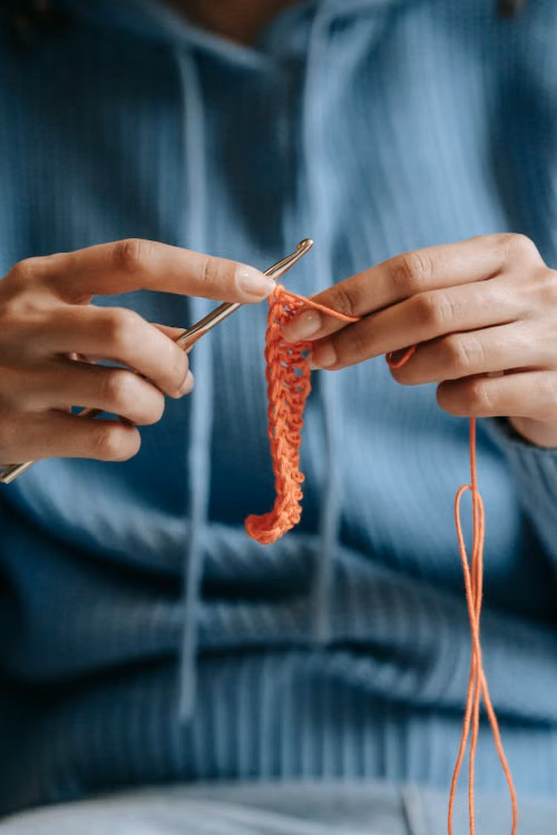 Hands crocheting orange yarn - close up of crochet vest stitches in progress